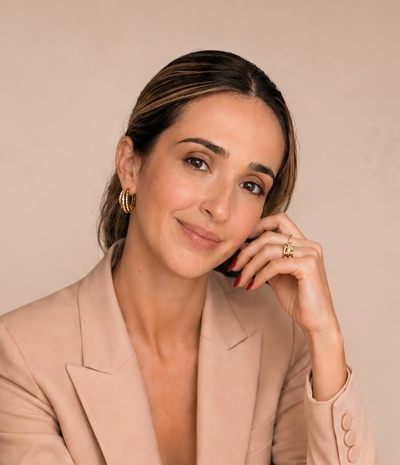 Carol Bressan de blazer nude, com a mão no rosto, sorrindo